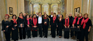 Grupo de pessoas vestidas maioritariamente de preto com lenços vermelhos, posando em fila no interior de um edifício histórico, em fotografia de grupo.